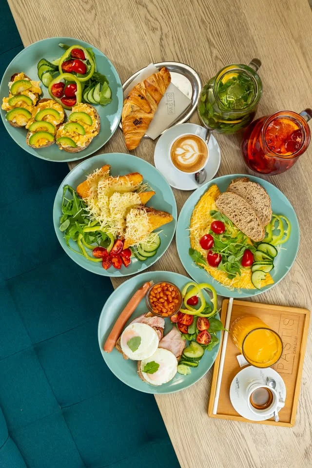 Stôl plný raňajok — vajíčka, croissant, zelenina, džús a káva
